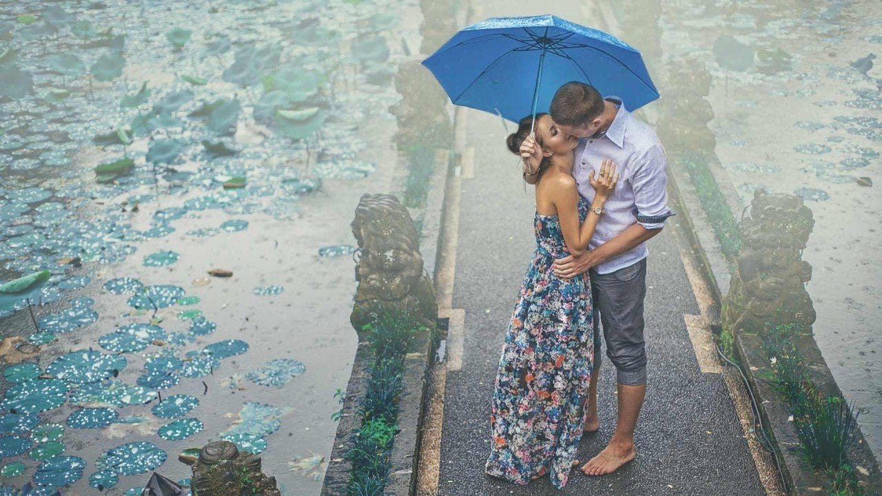 A couple standing in romantic embrace under an umbrella by a lilly pond in Bali