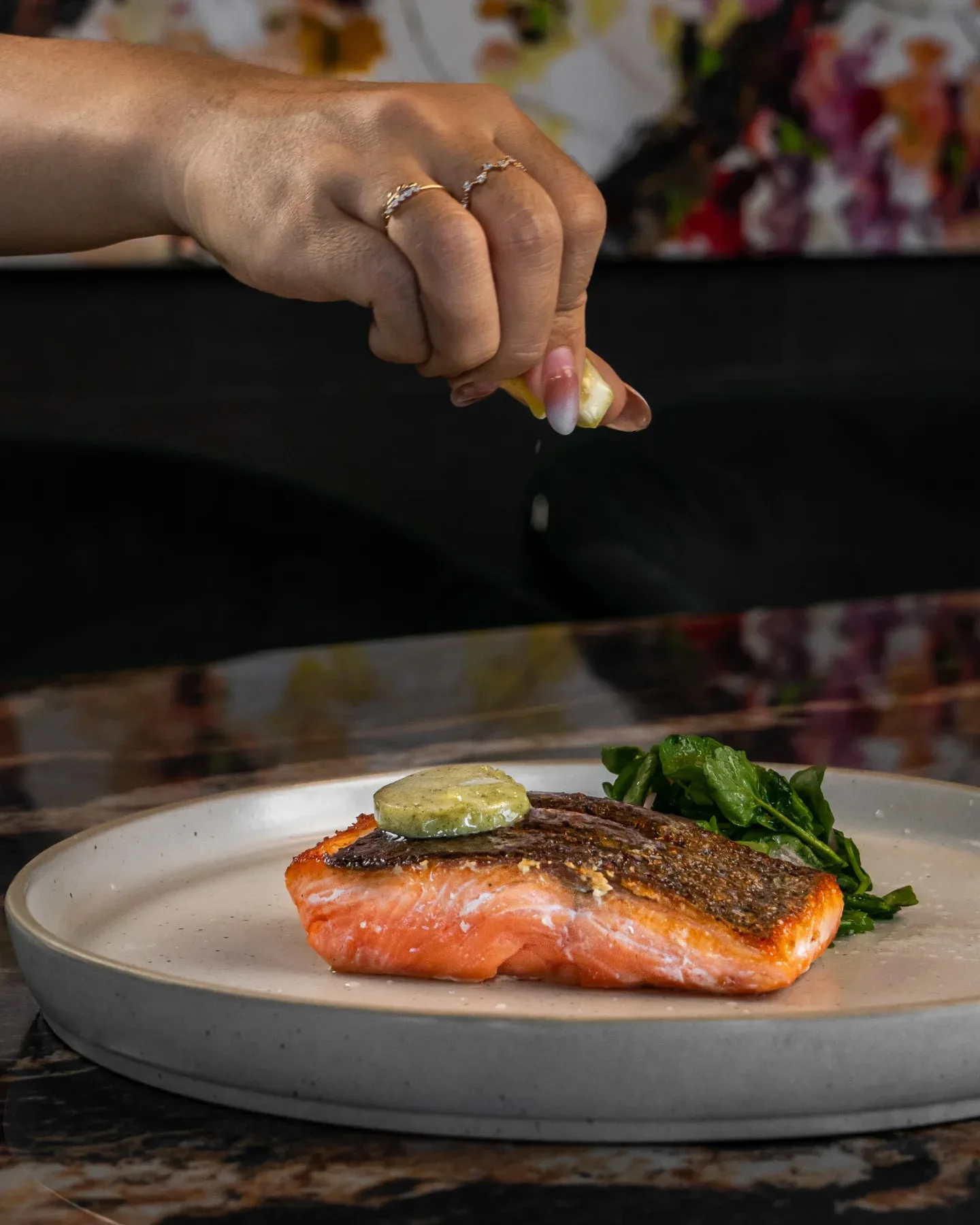 A catering chef in Canggu squeezing lemon to a finished plate of salmon with salad garnish