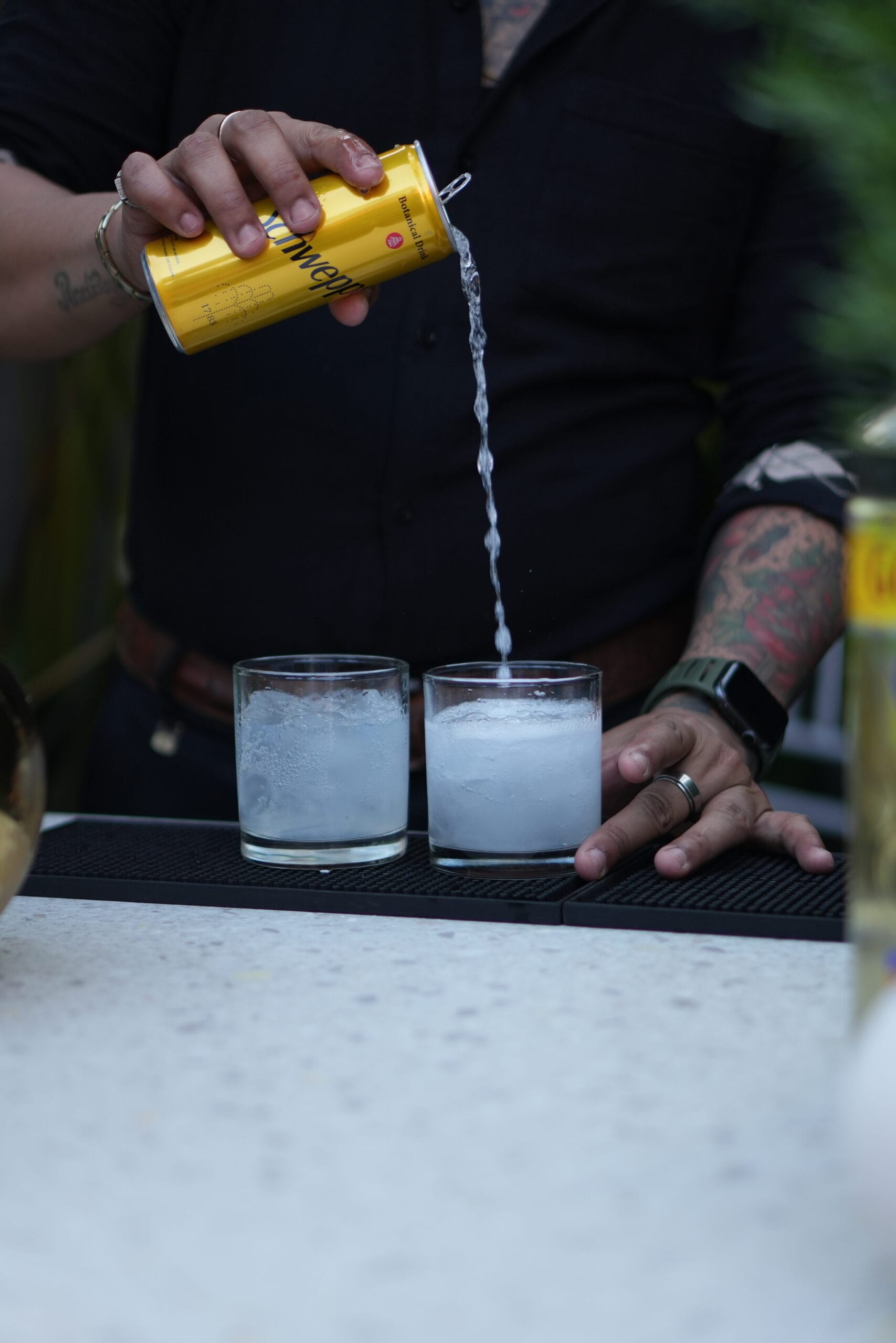 A bartender pouring tonic water into two glasses